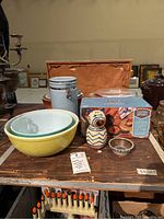 Overview of set including Pyrex mixing bowls, stoneware crocks, ceramic canister, Pfaltzgraff creamer, small bowl, and Berkley Jensen spice container box on wooden table.