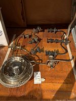 Several silver plated candelabra tops and curved arms laid out on a wooden surface showing tarnish and wear.