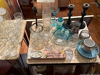 Full overview of glassware, candlesticks, ceramic pitcher and dishware on wooden surface