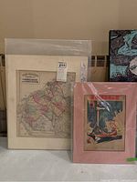 Two vintage maps and one Judge magazine cover matted and displayed standing against a wall.