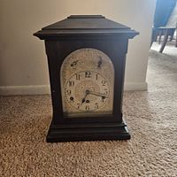 Front view of antique stationary chime clock showing wooden case, dial with Arabic numerals, and two winding holes.