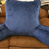 Navy blue fluffy-armed bed rest pillow photographed on a brown couch.