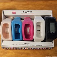 Photo shows B-Active main fitness tracker unit and four interchangeable multicolored wristbands in packaging.