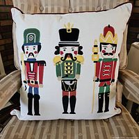 Square pillow featuring three colorful nutcracker soldier prints on cream fabric with dark piping trim.