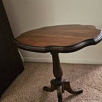 Photo showing the side table with the top open, displaying the scalloped oval wooden surface and tripod base.