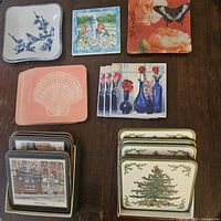 Photo shows multiple sets of coasters arranged on wooden surface, featuring various designs and themes as described in the seller description.