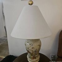 Full view of the porcelain table lamp showing the floral and bird design on the base, white fabric shade, and gold finial.