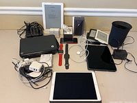 Overview of lot showing HP laptop, Kindles, tablets, watches, smartphone, cables and Google Nest box
