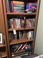 Full view of oak finish bookshelf with several shelves holding mixed assortment of books and games.