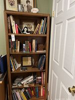 Books arranged on five-shelf wooden bookcase showing variety of book genres and some decorative items.