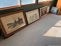 Five framed art prints leaning against wall on carpeted floor in natural light