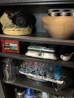Photo of wooden shelf cabinet with kitchen and baking items including baskets, bowls, a scale, glassware, and pans.