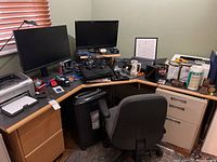 Corner desk surface with printer, monitors, laptop and chair