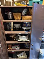 Image of the metal cabinet with shelves filled with kitchen baskets, pots, tins, and ceramic dishes.