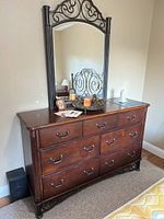 Wooden dresser with nine drawers and decorative iron-framed mirror attached, shown from front angle with items on top.