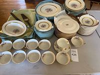 Set of multiple Gainsborough china pieces including plates and teacups arranged on a table with protective cloths and baskets.