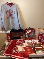 Photo of XL gray 49ers sweatshirt hanging on the wall with memorabilia and bags arranged on table in front