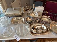 Full view of the silver plated serving pieces including trays, bowl, candelabra, cutlery set, and crystal dishes on a table.