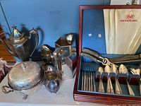 Photo showing silver plated coffee pot, creamer, covered serving dish, and wood box with flatware inside.