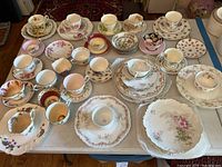 Overhead photo of a collection of 25 assorted vintage teacups, saucers, and small plates arranged on a table.