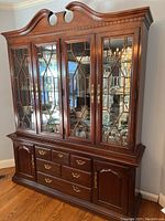 Full view of Thomasville china hutch showing upper glass cabinet with wooden lattice, lower storage with drawers and cabinets, brass hardware, and dark wood finish on hardwood floor.