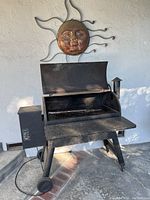 Overall view of pellet grill and metal sun wall art mounted above