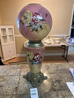 Full front view of vintage lamp showing painted floral globe and ornate metal base on granite counter.