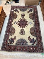 Full view of area rug showing ivory background, red border, medallion and paisley motifs and fringe
