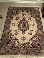 Full view of beige area rug with intricate floral medallion and border design, tassels visible on one end