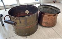 Overview of the two pots side by side showing size difference and material contrast with wooden handles on the larger pot