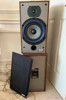 Pair of speakers with one fabric cover removed showing front drivers and bass port