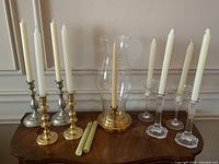 Full display of four pairs of candlesticks and tall hurricane with candles on a wooden surface.