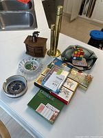 Lot arranged on white countertop showing ashtrays, cribbage, wooden box with coasters, brass tone change sorter, playing cards, and decorative wooden cabin.