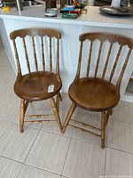 Two wooden dining chairs with round seats and spindle backs shown from the front near a kitchen counter.