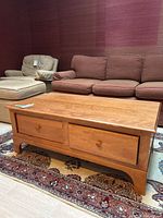 Light wood rectangular coffee table, front view showing two drawers and wooden knob handles, positioned against sofa.