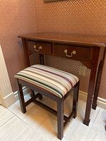 Wooden console table with two drawers and matching bench with striped fabric seat positioned underneath, showing overall appearance.