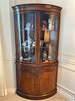 Full view of mahogany finished corner cabinet with curved glass doors and lower storage doors, showing the overall shape and condition.