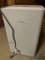 Front angle view of white rectangular NOMA dehumidifier with power cord attached, showing overall condition and size.