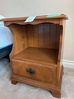 Front view showing the open shelf, bottom drawer with metal handle, and scalloped trim on top edge.