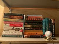 Full view of stacked hard cover books and signed baseball base on a shelf