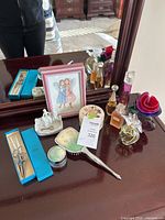 Overview of lot items on dresser including perfume bottles, framed art, nail kit, vanity mirror, jars, rose dishes, porcelain dish figurine