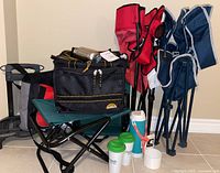 Photo of entire lot showing folding chairs, folding stool, cooler bag with wheels and handle, thermal bags, a thermos, and drinkware.