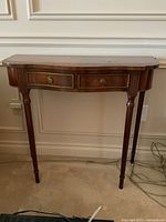 Front view of the wooden side table against the wall showing its curved front and two drawers.