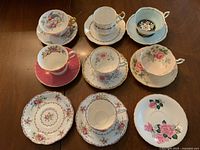 Top-down view showing seven teacups each paired with matching saucers, displaying a variety of floral bone china patterns and gold accents.