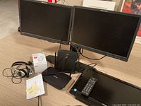 Two Lenovo computer monitors side by side, Linksys router, wired headphones, Toshiba TV remote and TV.