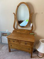 Front view of washstand showing wood finish, three drawers, oval mirror and lion head ring pulls
