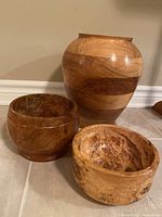 Overall view of the large willow urn standing behind two smaller burled wood bowls on tiled floor