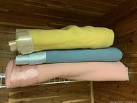 Three folded wool blankets stacked: yellow on top, blue middle, pink bottom, all with satin trim edges.