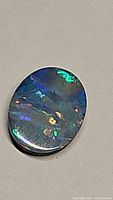 Oval black Australian opal doublet displaying vibrant blue, green, and orange play of color on a smooth polished surface.
