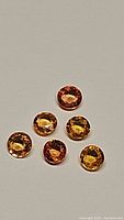 Photo of six round faceted sapphires in orange to yellow tones on a neutral background.